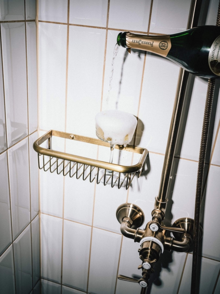 Ein Champagnerglas wird in einer Dusche gefüllt, während eine Flasche Champagner über das Glas gelehrt wird.
